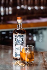 William Whipple's Winter Wheat Whiskey bottle next to cocktail with orange peel.
