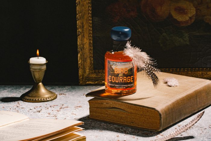 Bird of Courage bottle on top of vintage book in front of vintage painting and lit antique candle.