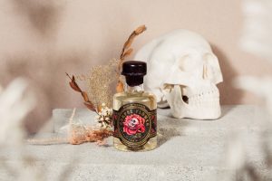 Corpse flower durian brandy in front of dried flowers and white skull. Light pink backdrop.